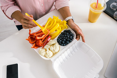 在食品容器中，妇女手持塑料叉子靠近蔬菜的顶视图 