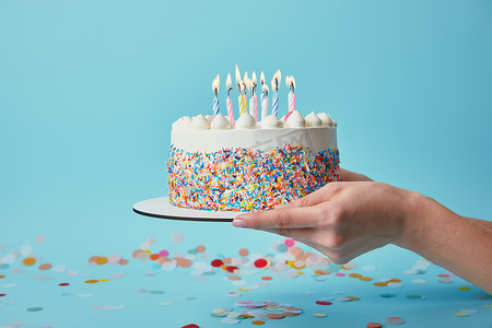 妇女拿着生日蛋糕与蜡烛在蓝色背景与五彩纸屑的部份看法