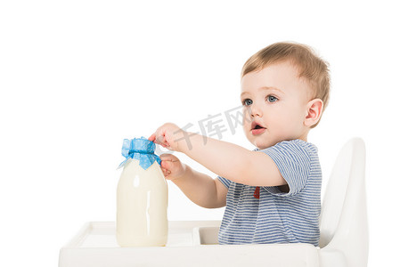 可爱的小男孩与瓶牛奶和坐高脚隔绝在白色背景 