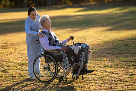 坐在草地摄影照片_护士陪伴坐在轮椅上的老年人