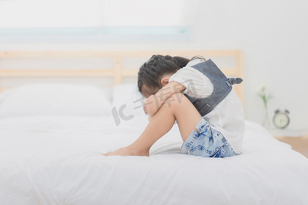 坐在床上，她抱着膝盖在难过的时候喜怒无常的郁闷亚洲小女孩.