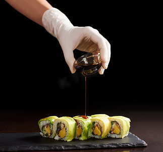 滚动寿司制作过程的特写视图。手手套倒入美味的新鲜面包酱。深色背景
