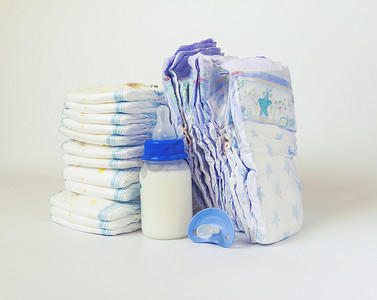 纸尿裤一袋摄影照片_堆纸尿裤和白色背景上的婴儿奶瓶.
