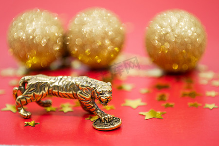 A bronze figure of a tiger with a coin - the symbol of the Chinese new year 2022 on a red background, gold stars and balls, a copy space.