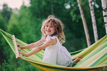 happy child girl relaxing in hammock on summer camp in forest. Outdoor seasonal activities for kids.