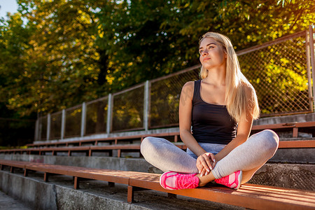年轻女子运动员在夏天运动场跑步后休息。快乐的女孩坐在板凳上放松锻炼后