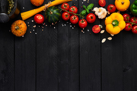 食物背景为美味的意大利菜, 西红柿, 辣椒粉, 南瓜和大蒜。各种烹饪配料, 意大利面在黑色木桌上。带复制空间的顶部视图.