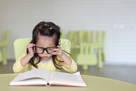 孩子们的房间摄影照片_聪明的小女孩戴着眼镜, 打算在孩子们的房间里看书.