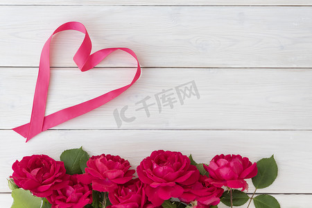 roses摄影照片_Top view of red roses on bottom and heart shape made from ribbon on white wooden background, greetings and holiday concept