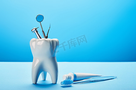 不锈钢背景摄影照片_在蓝色背景下, 可近距离查看白色牙齿模型、牙刷、牙膏和不锈钢牙科器械