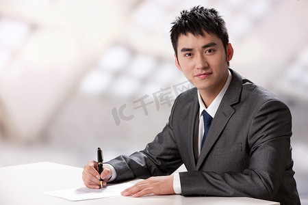 拿笔写字背景摄影照片_青年商务男士在办公室里写字