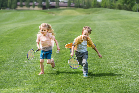 可爱的微笑儿童与羽毛球球拍一起跑在公园 