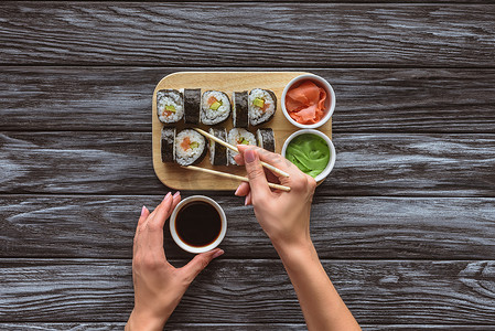 在吃寿司时手持筷子、碗和酱油的人的部分顶级视图 