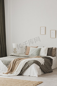 毯子和枕头在床上, 在白色的最小卧室内部与地毯和海报。真实照片