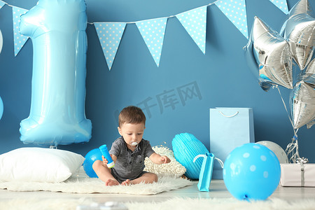 可爱的小男孩坐在地毯上装饰的第一个生日聚会的房间