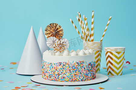 美味的蛋糕, 平静的杯子, 派对帽和喝吸管蓝色背景与五彩纸屑