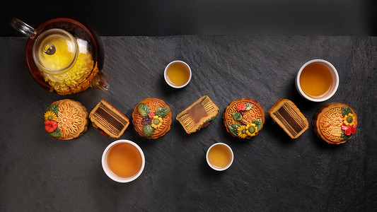 五彩缤纷的月饼中国中秋节装饰在黑色石板背景的小白瓷茶壶上