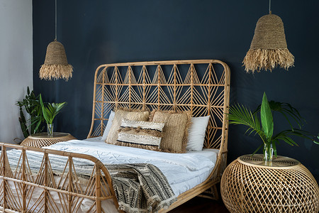 点波摄影照片_波希米亚风格的室内舒适的房子与少数民族装饰。精致的卧室，床头柜上方点着灯，舒适的床上有枕头，有仙人掌植物，还有深蓝色墙壁上的空间