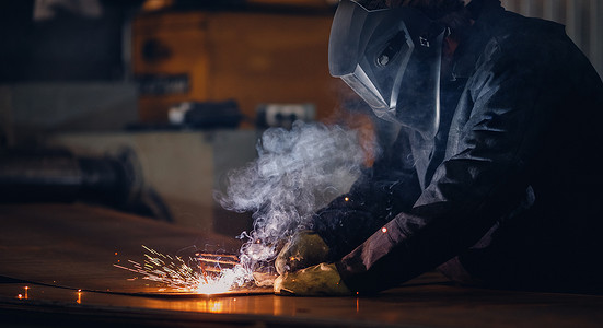 专业焊工在防护服与面罩，火花飞散，工业焊接特写