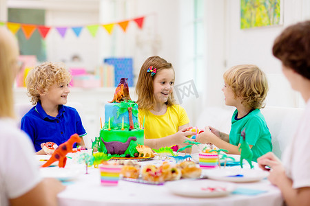 孩子们的生日派对恐龙主题蛋糕。小女孩吹蜡烛和打开礼物。儿童活动。恐龙装饰主题庆祝活动.