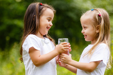 两个小女孩在绿色公园里喝着一杯水。纯净、生态和生物产品的概念, 对自然的爱