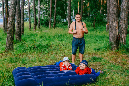 夏天, 一个男人带着两个孩子在树林里抽着蓝色的气垫床垫。