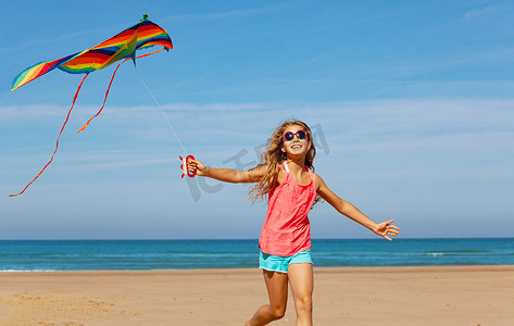 一个美丽、快乐、无忧无虑的姑娘牵着放风筝跑在沙滩上的亲密画像