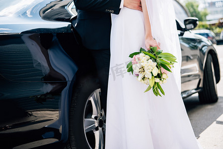 裁剪视图新郎在西装拥抱新娘在婚纱与花束