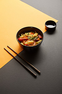 酱油河蟹摄影照片_在筷子附近的碗里放有虾仁和蔬菜的面条，黑黄相间的酱油