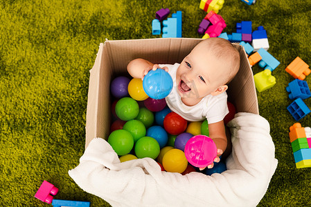 快乐的小孩坐在纸板箱里玩五颜六色的球