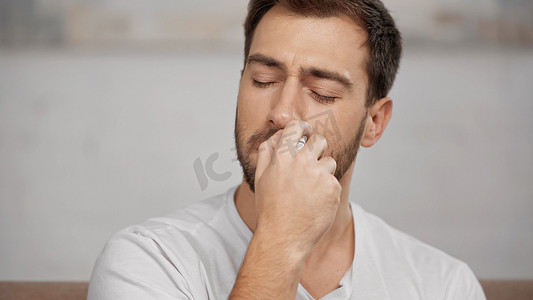 spray摄影照片_allergic man in white t-shirt using nasal spray at home 