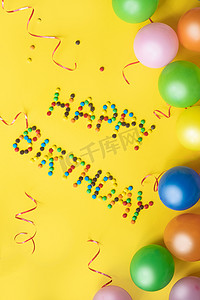 快乐的生日信从糖果。生日背景。黄色桌子上的彩色气球和糖果.