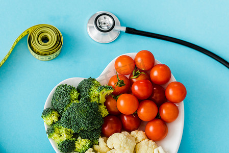 美味的有机蔬菜在心形板附近测量胶带和听诊器在蓝色