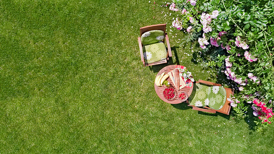 在美丽的夏季玫瑰花园装饰了面包、草莓和水果的餐桌，空中俯瞰着从上方为两人准备的浪漫约会餐桌食物