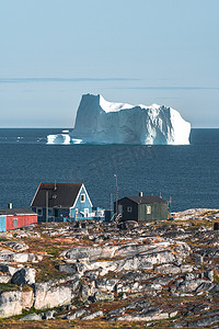 色彩斑斓的蓝色木制房屋，背景上有冰山。 Rodebay也被称为Oqaatsut，是Ilulissat以北的一个渔业定居点。 迪斯科湾和盖克尔塔苏克。 蓝天和太阳.