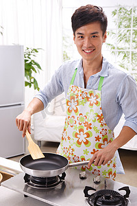 俯视俯视锅摄影照片_一个年轻男人在厨房做饭