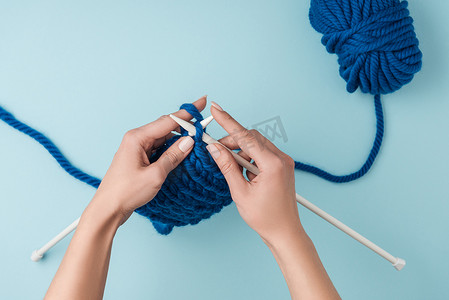 裁剪拍摄的妇女编织在蓝色背景与蓝色纱线