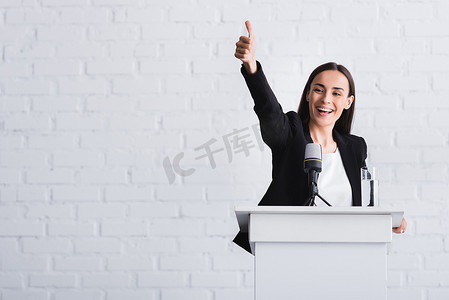 讲台上摄影照片_快乐，有吸引力的讲师显示竖起大拇指，而站在讲台上