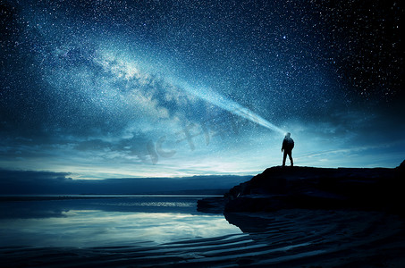 一个人站在那里看银河星系上升到夜空。照片合成