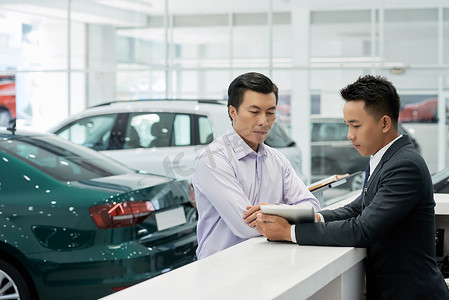 汽车经销商的年轻专业销售经理向客户展示平板电脑上的合同细节