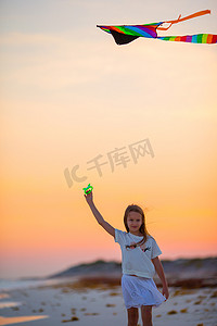 在日落时分在热带海滩上放风筝的小女孩。在大洋彼岸打孩子。儿童沙滩玩具.