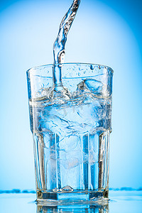 装冰块的杯子摄影照片_把清澈的水倒入一个杯子里，杯子里装的是蓝色坡度背景的纯冰块