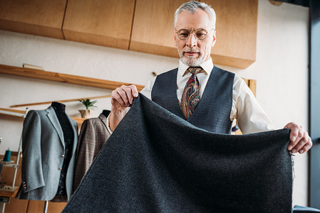 裁缝店海报摄影照片_缝纫车间用灰色布料的英俊成熟裁缝