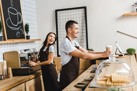 一摞纸杯摄影照片_英俊的收银员给纸杯有吸引力的咖啡师在咖啡屋的酒吧柜台后面微笑