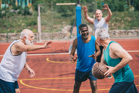 跨种族的老年运动员在操场上一起打篮球