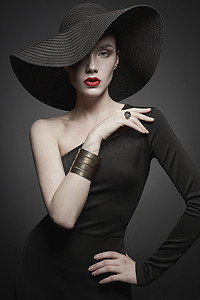 黑色背景摄影照片_带黑色帽子和晚礼服的年轻女士的肖像