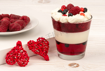 and摄影照片_Sweet dessert in glass with cream, jell, raspberries and blueberries on wooden background.
