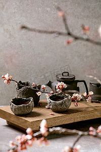 茶喝的是日本风格的芥末砂浆杯和茶壶，放在开着樱花枝条的木制茶几上。灰色纹理混凝土背景.