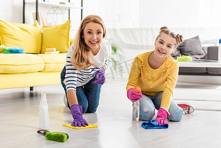 妈妈和女儿拿着喷雾器和抹布擦地板，笑着看着镜头靠近客厅里的刷子