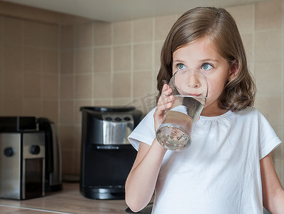 小孩子正在家里喝干净的水,特写。白种人可爱的女孩长头发是在她的手中拿着一个水杯。照顾好自己的健康。健康的生活方式理念,良好的习惯